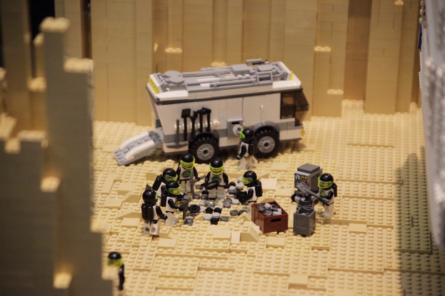 Lego-Modell einer Star-Wars-Szene mit einem Landfahrzeug im Vordergrund und einer Wand im Hintergrund sowie ein paar verstreuten Spielzeugen.