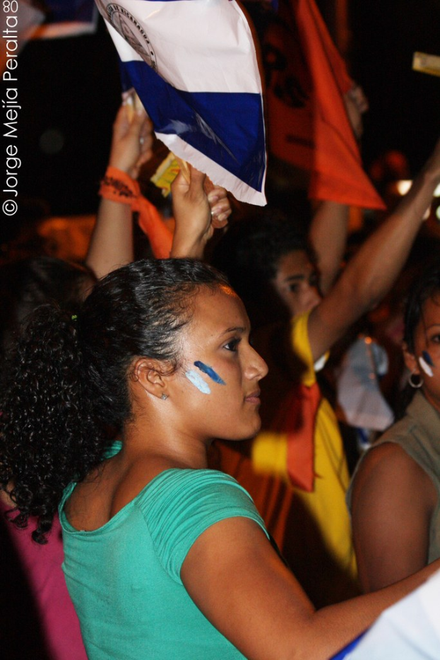 Frauen in grünen T-Shirts bei einer Demonstration, die weiße Abdeckungen halten, mit mehreren Mädchen dahinter.