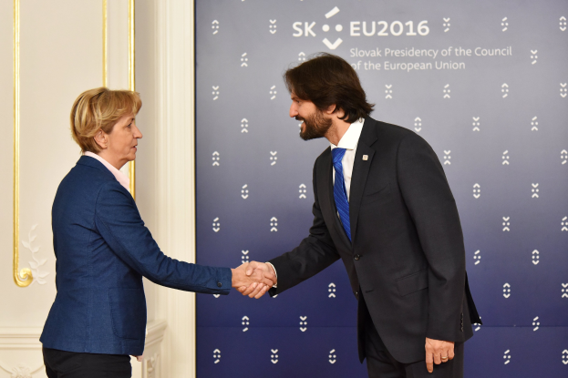 Bundeskanzlerin Angela Merkel und Bundespräsident Joachim Gauck schütteln sich lachend vor einer Wand mit einem "EU-Gipfel"-Schild und einer Tür die Hände.