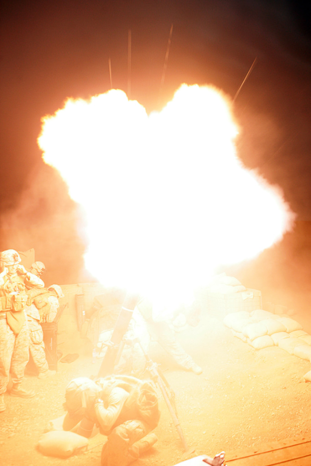 Mehrere Personen in Uniformen und Helmen befinden sich auf einem Gelände mit Taschen, wobei ein Feuer in der Mitte der Szene zu sehen ist.