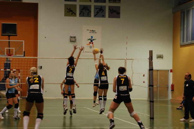 Ein Volleyballfeld mit aktiv spielenden Spielern, mit einem Basketballnetz, Fenstern und einer Tür im Hintergrund.