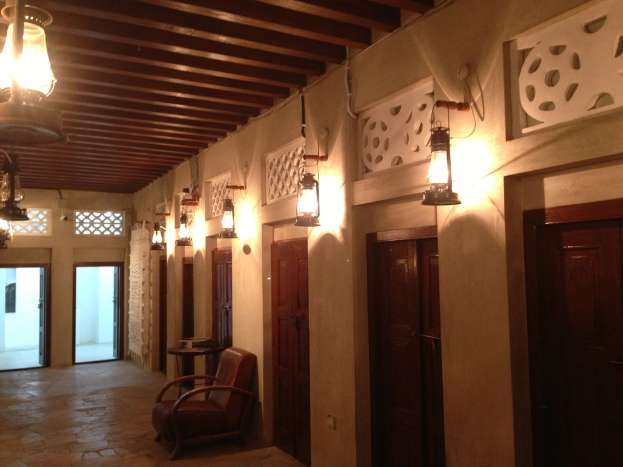 Ein Gebäude mit geschlossenen Räumen, jeweils mit einer wandmontierten Lampe und einem Deckenventilator, einem Stuhl davor und zwei Eingängen, mit zusätzlichen Lampen an der Decke.