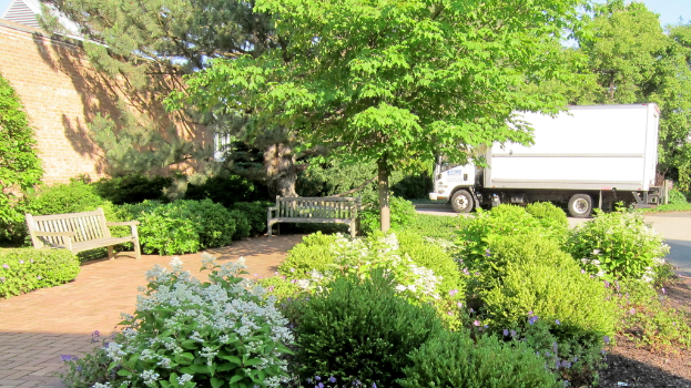 Ein Lastwagen steht neben ein paar Bäumen, Bänken und blühenden Pflanzen.