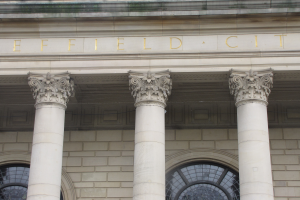 Ein prächtiges Gebäude mit hohen, schlanken Säulen und einem mutigen Schild, auf dem "Effield City Hall" steht, umgeben von üppiger Vegetation.