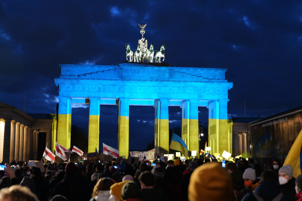 Menge mit Fahnen und Schildern vor dem Reichstagsgebäude, mit einer Fahne auf der rechten Seite des Bildes.
