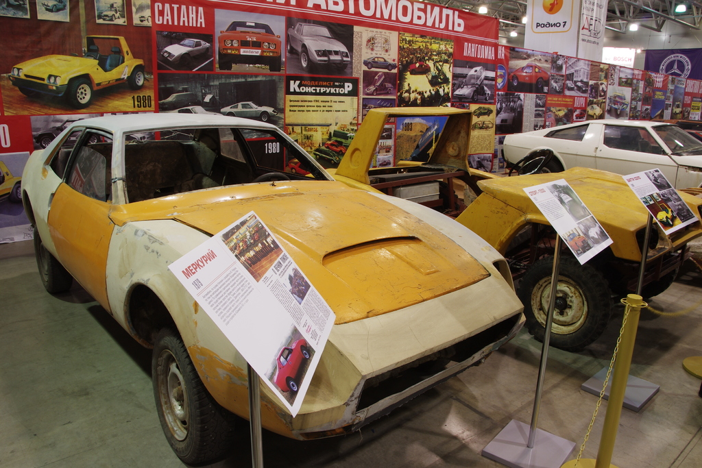 Ein Parkplatz mit mehreren Autos, Stände mit Plakaten und ein großes Plakat im Hintergrund.